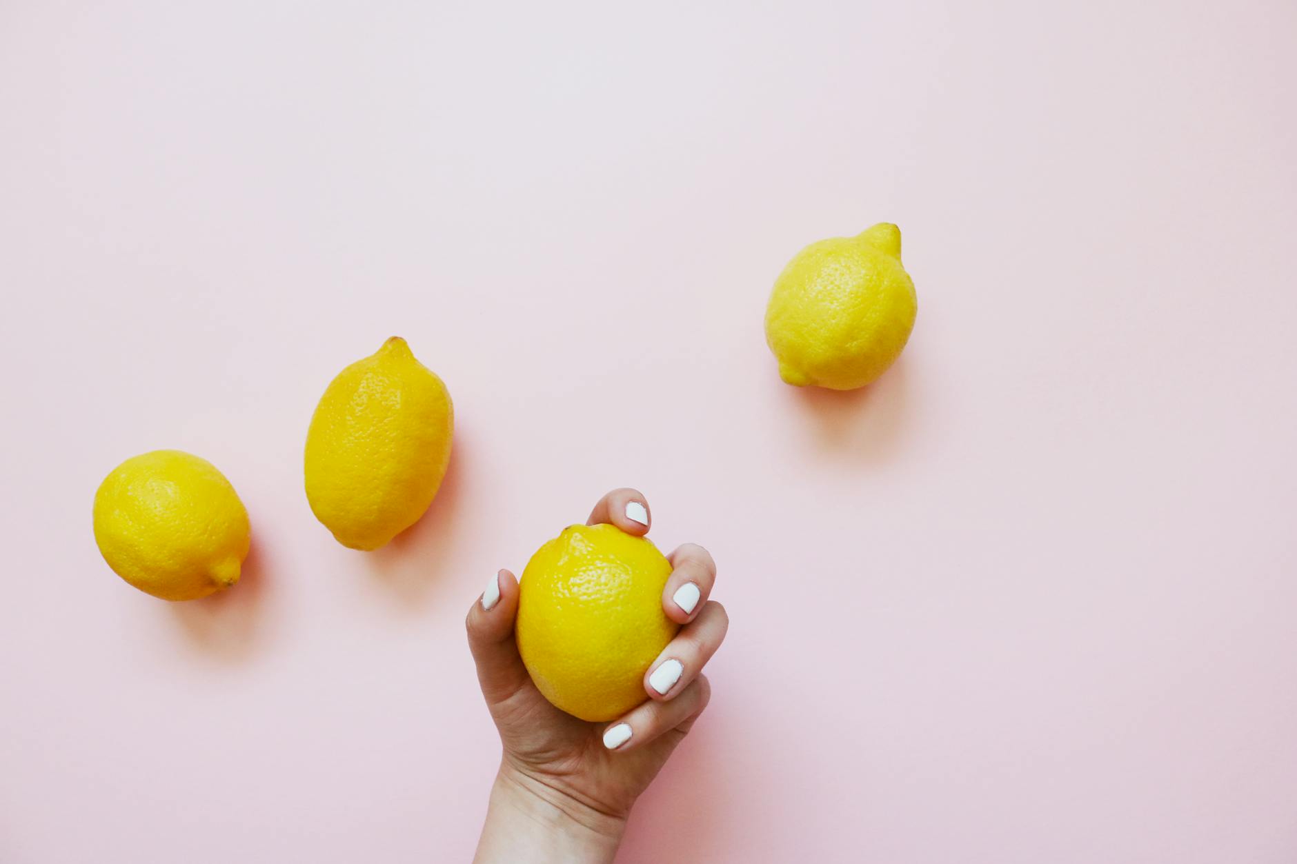 Hand holding a fresh lemon on soft pink background, representing clitoral sensitivity and renewal