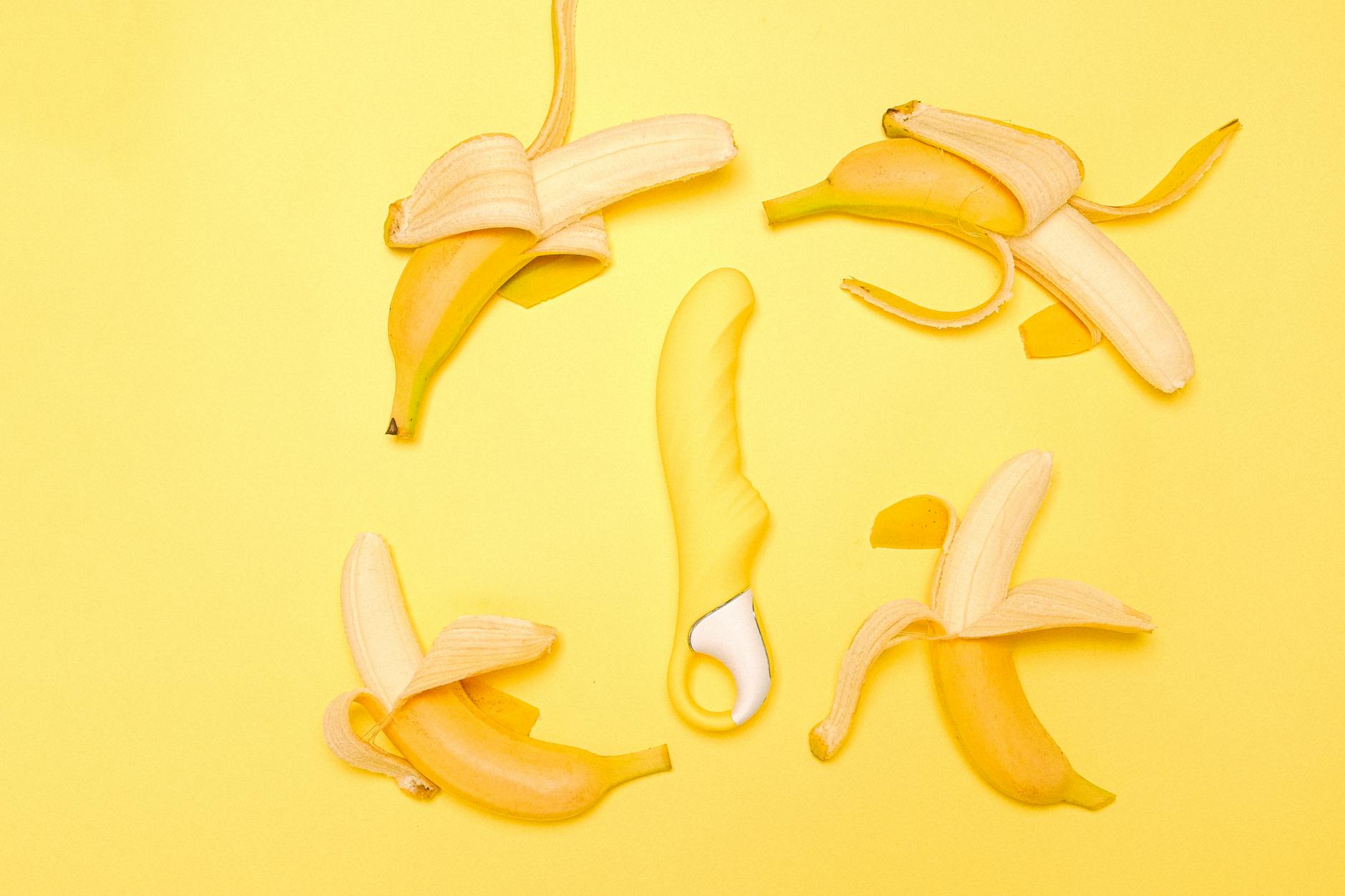 A bright yellow silicone clitoral vibrator surrounded by fresh lemons on a yellow background