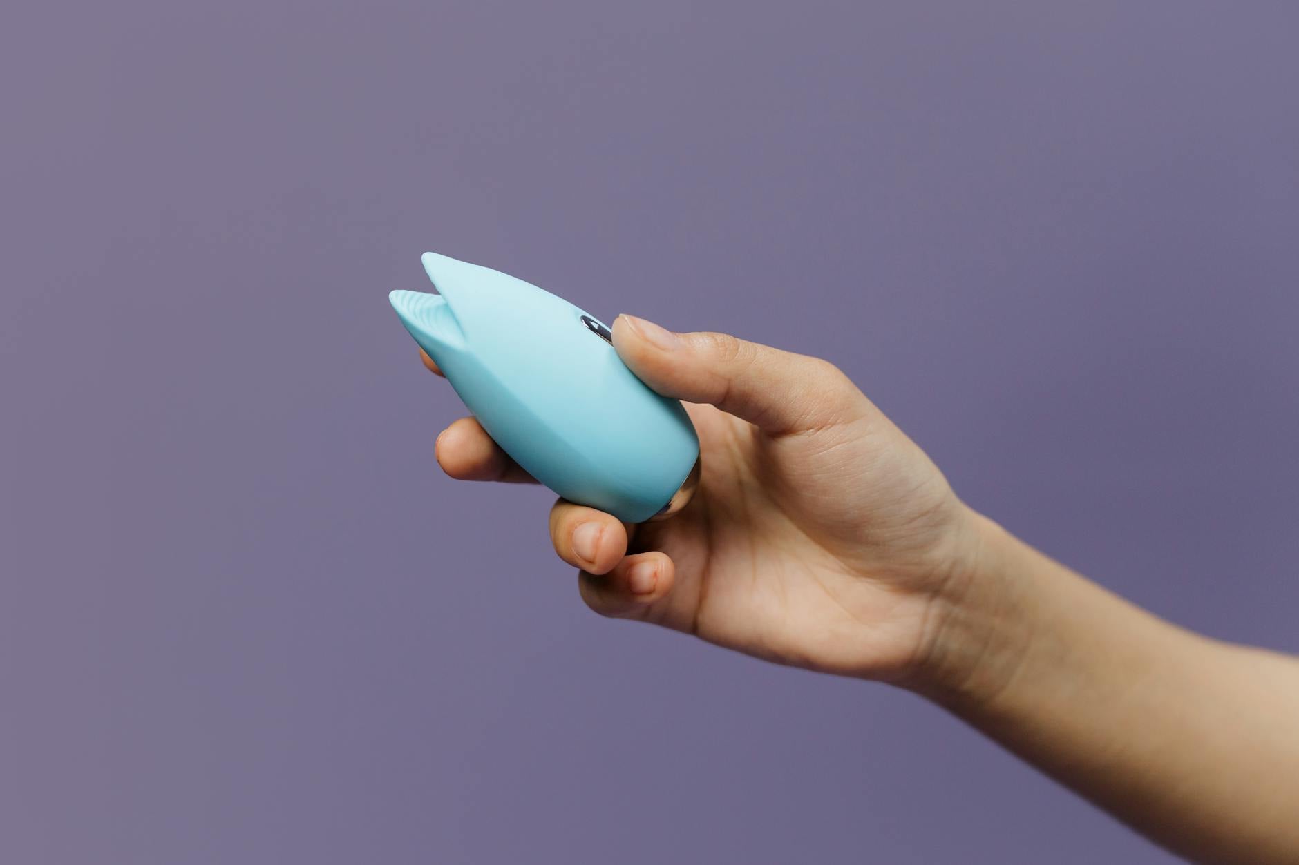 Close-up of a blue silicone clitoral vibrator held in hand, symbolizing self-care and personal pleasure
