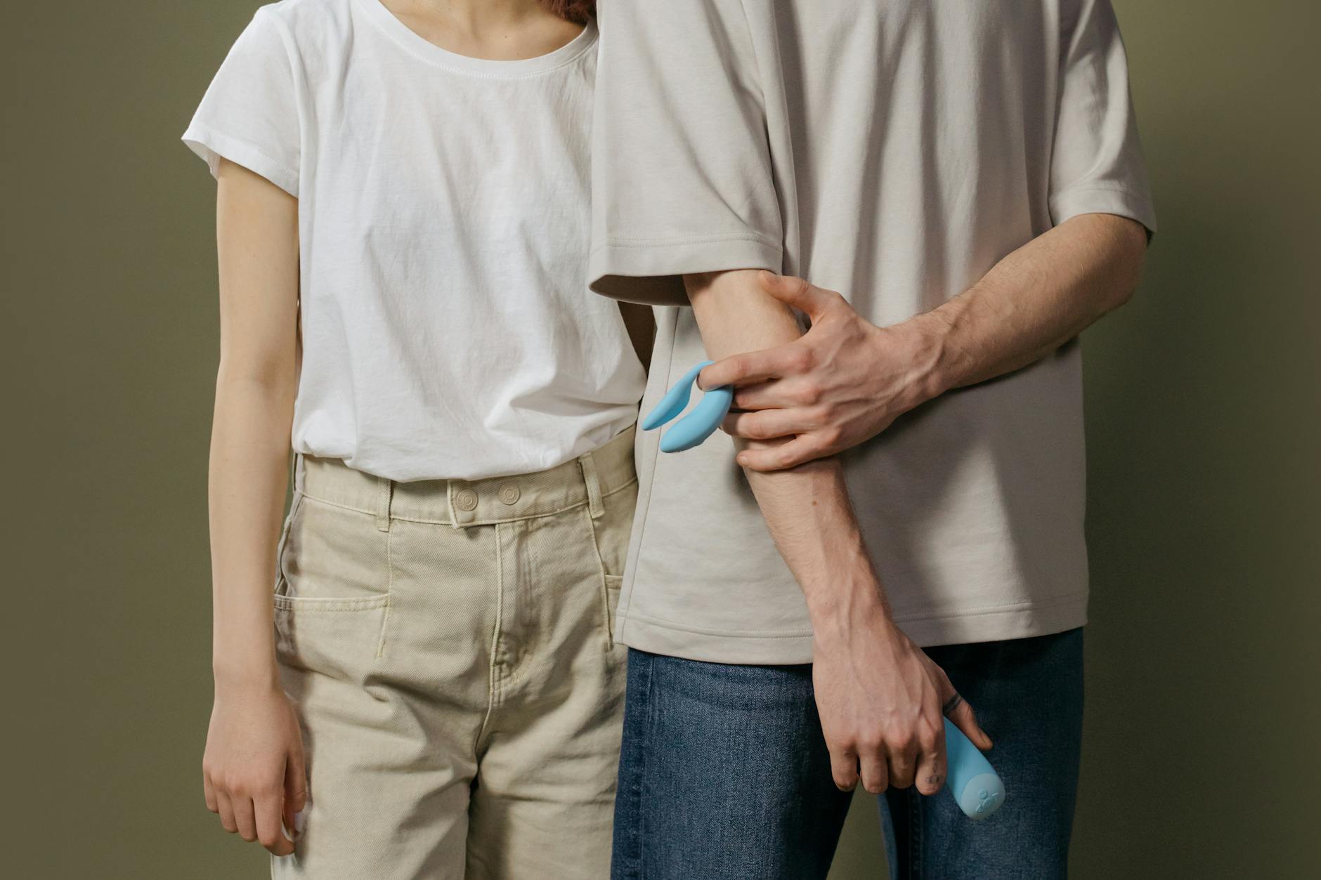 A hand holding a modern orange clitoral vibrator against a minimalistic purple backdrop