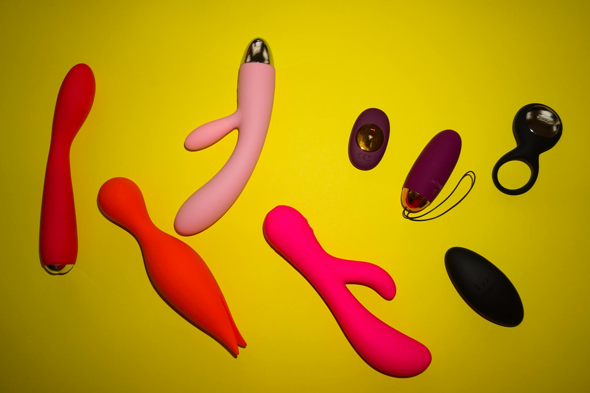 Vibrant collection of various clitoral vibrators in different colors arranged on a bright yellow surface